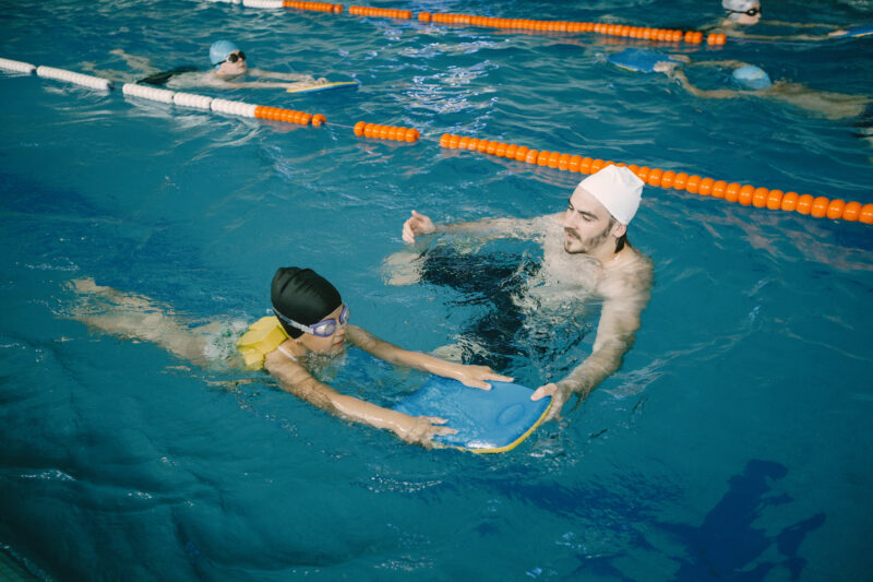 Mies opettaa uimahallissa lasta uimaan.